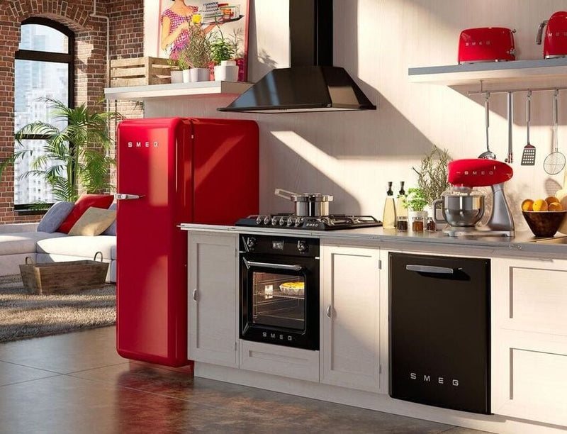 Modern kitchen with SMEG appliances including a red fridge, red toaster, red mixer, and black oven, set in a bright open-plan loft with exposed brick walls and plants.