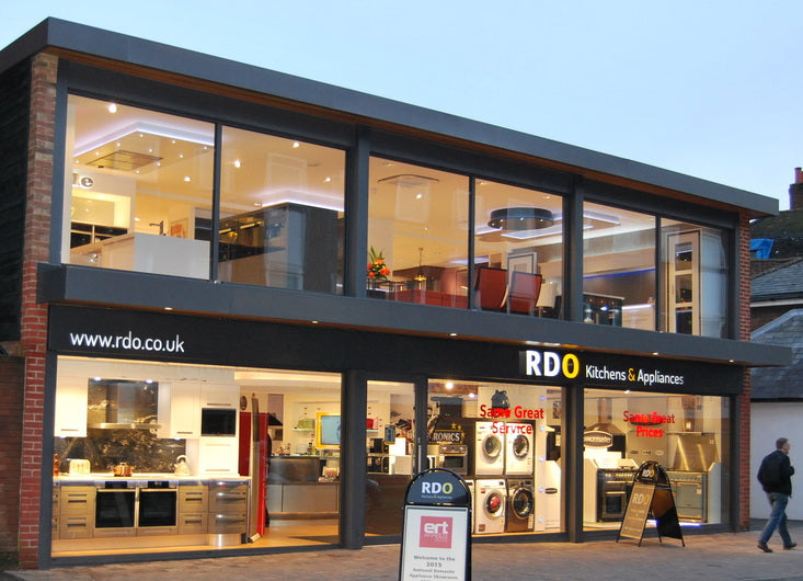 Exterior of RDO Kitchens & Appliances showroom in Reigate, Surrey, featuring illuminated modern kitchen displays and large glass windows.