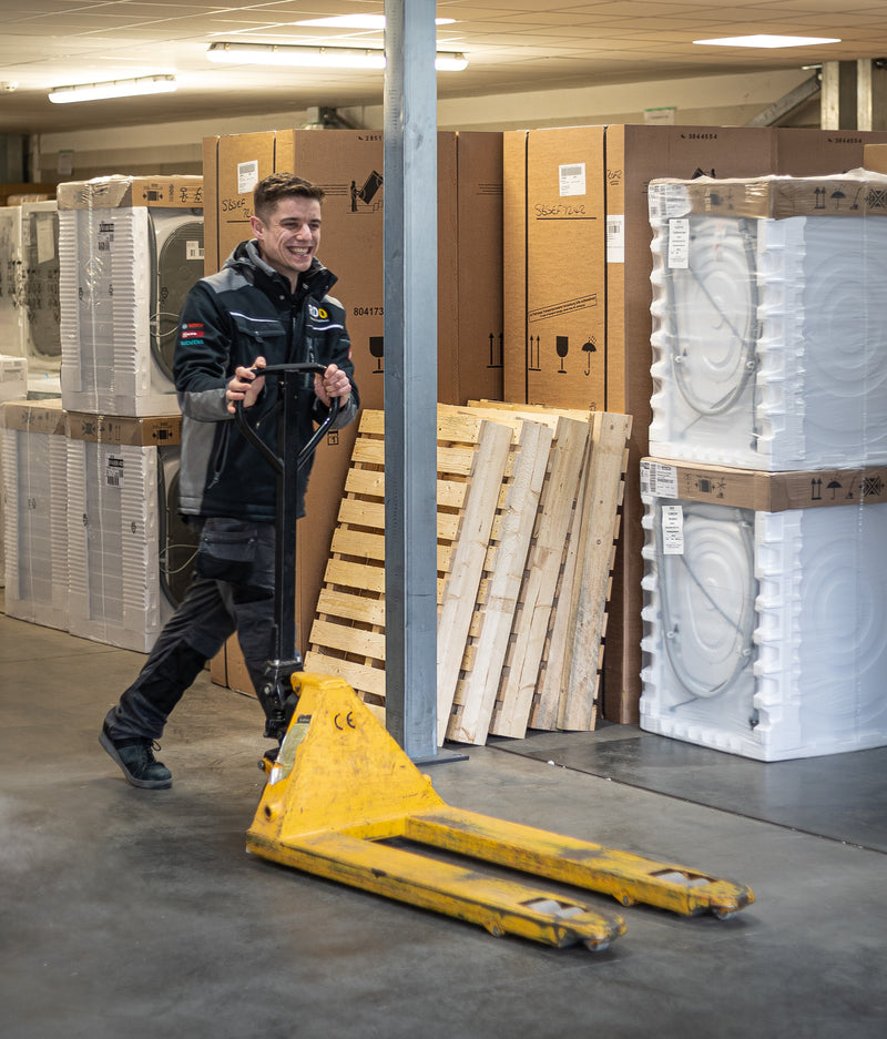 RDO warehouse team member smiling while moving appliances with a yellow pallet truck in a well-organised storage area.